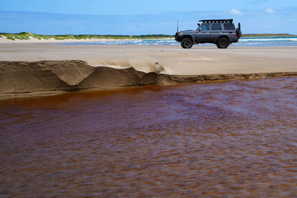 Mike Collister's Toyota LandCruiser 76 Series on a remote beach near Sandy Cape, north west Tasmania, with a tannin-stained creek in the foreground
