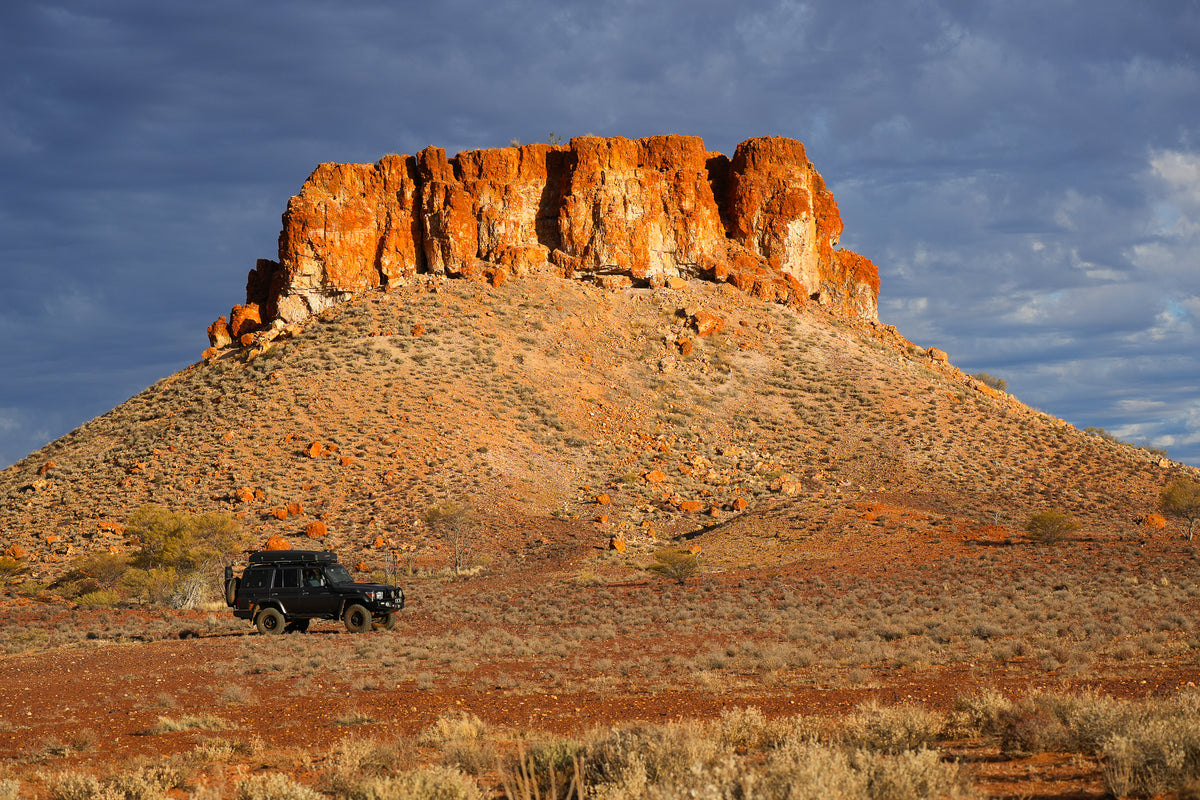 Mike Collister's Toyota LandCruiser 76 Series parked below a red rock mesa on the Anne Beadell Highway in remote Western Australia